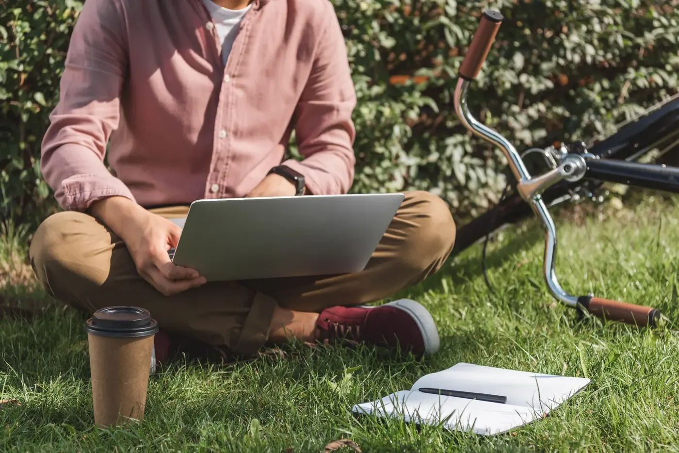 Freelancer working on a laptop outdoors on the grass with bike and coffee